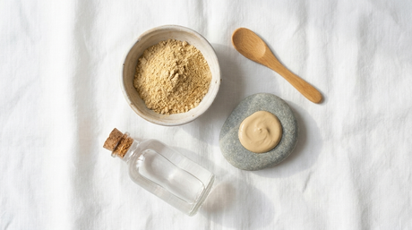 Multani mitti clay powder in a ceramic bowl with rose water and wooden spatula on white linen