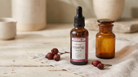 Bottle of Sampson Rosehip Face Oil styled with dried rosehip berries and an amber apothecary jar