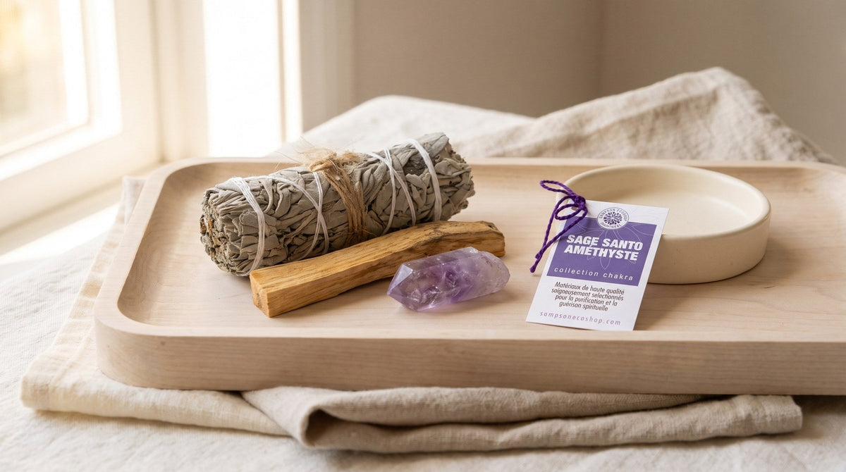 A white sage bundle, palo santo stick and amethyst crystal point with a purple Sampson Eco Shop card on a pale wood tray beside a cream ceramic dish, in soft window light